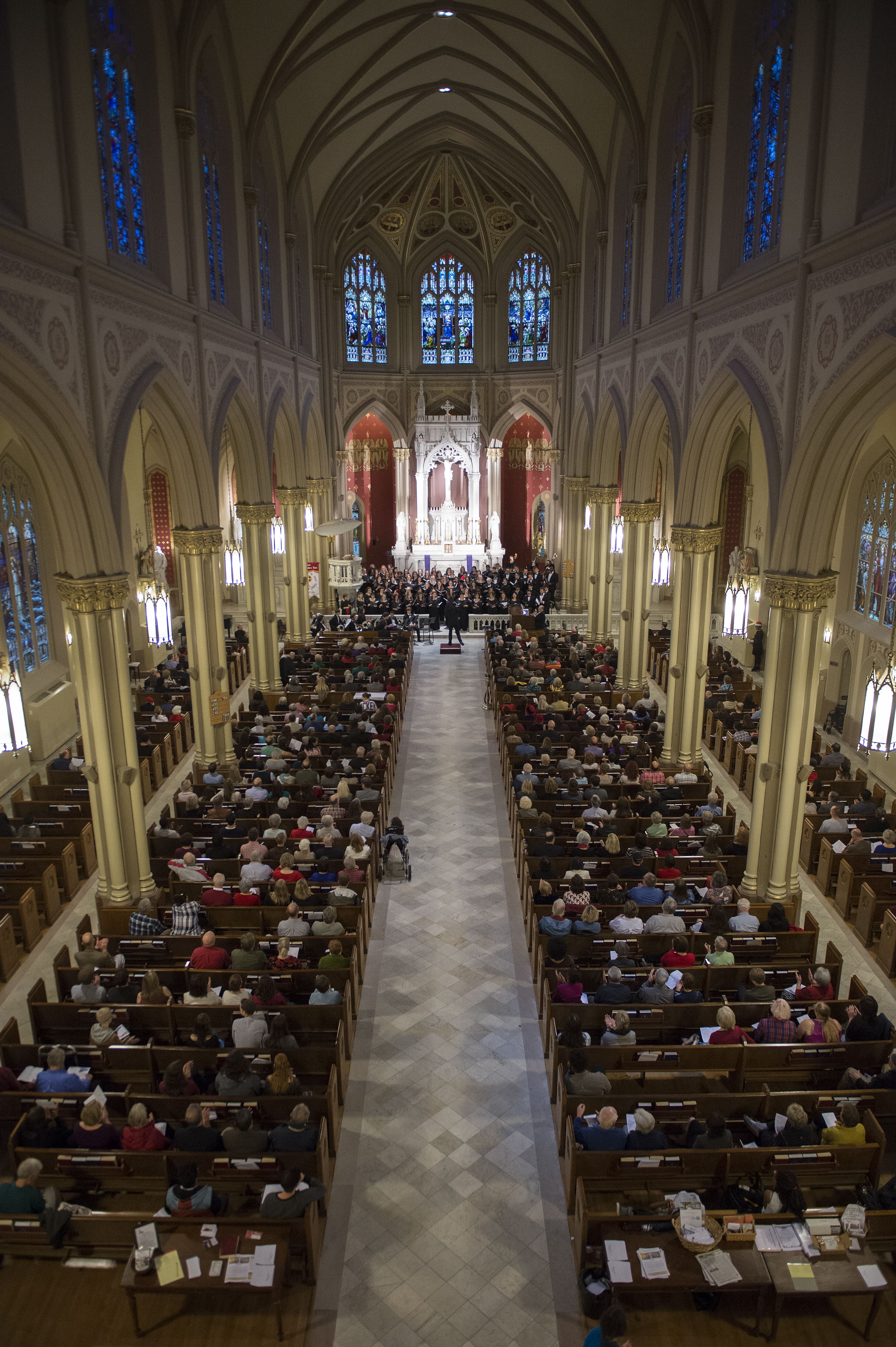 A high aerial shot of Holy Name of Jesus Church, filled with an audience listening to singers and instrumentalists performing on the altar.