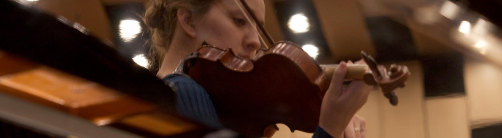 A reflection of a violin player performing, reflected off of the lid of a grand piano.