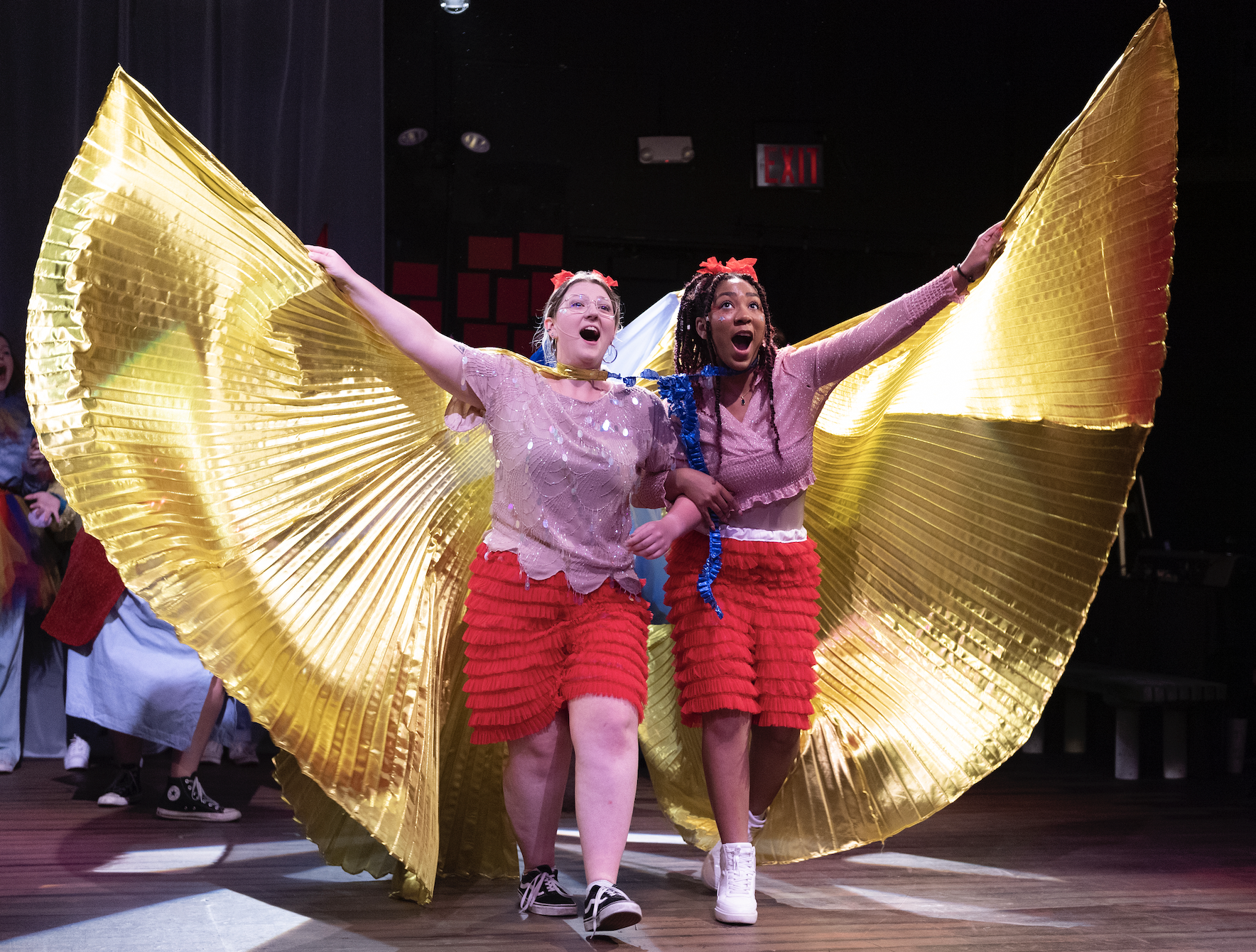 Two students hold up giant flowy, golden wings