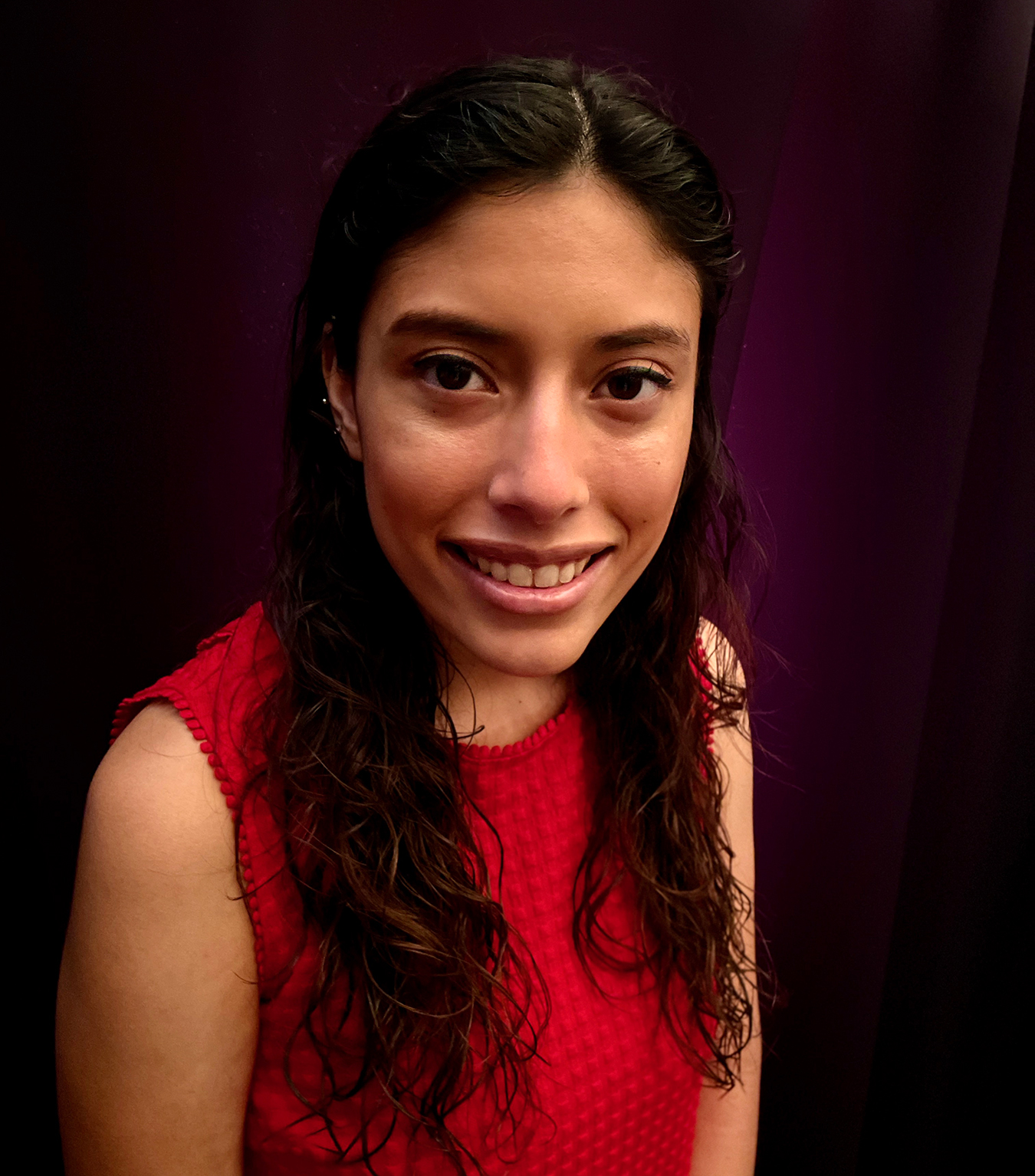 A young Mexican woman with long Black hair covering her shoulders smiles at the camera