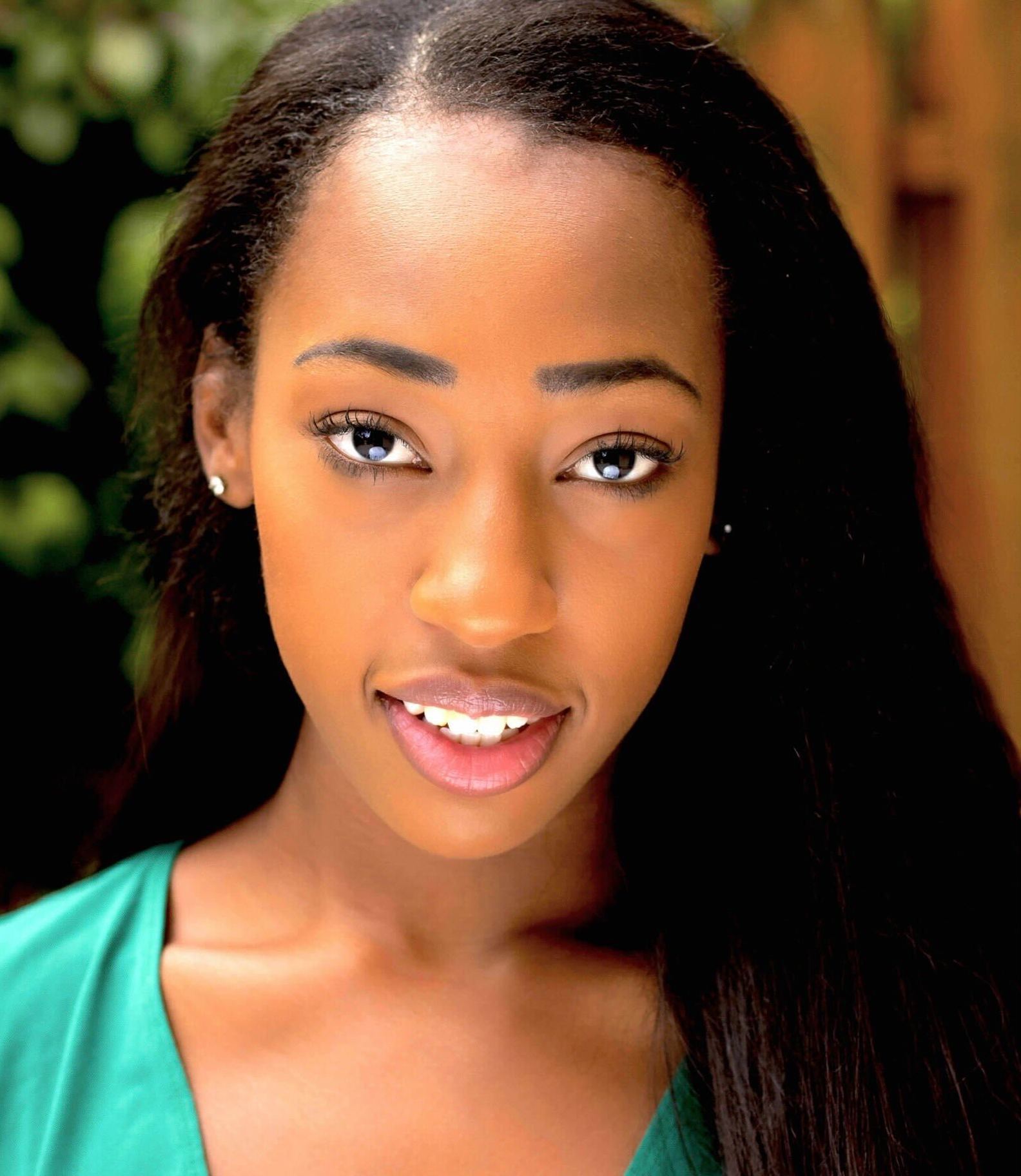 A young Black woman with a teal green sheet smiles at the camera