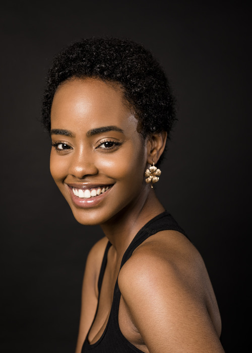 A young Black women with short natural hair smiles at the camera