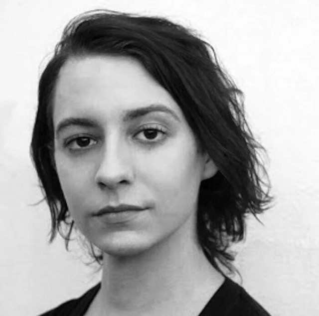 A white person with medium-length dark hair stares at the camera