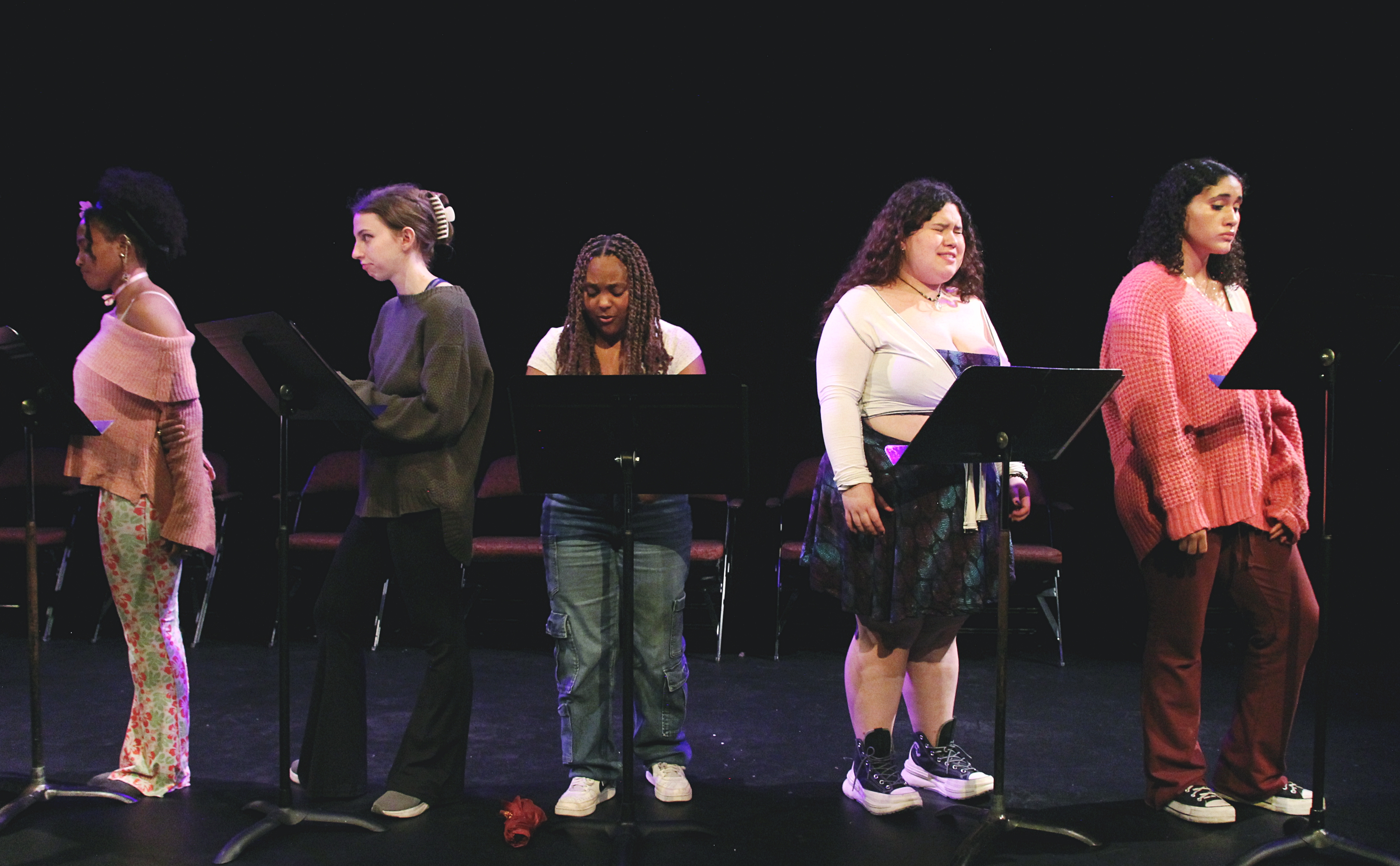 A group of young women stand in front of music stands in a theatre
